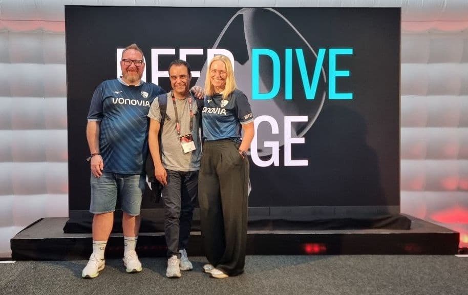 Three attendees in front of the Deep Dive stage at r26
